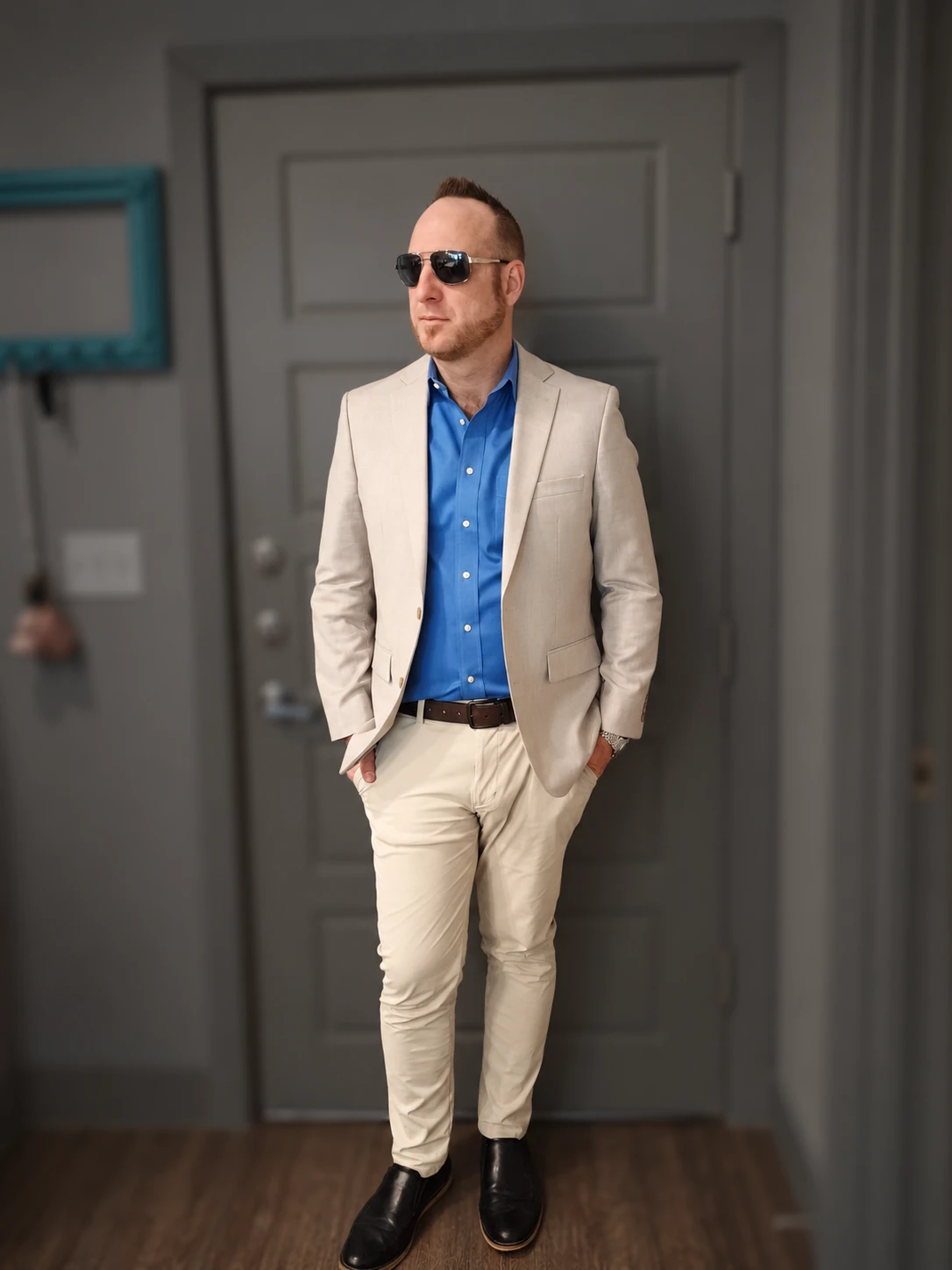 Sean Mansfield standing in a cream suit and blue shirt, with the apartment surroundings softly subdued.